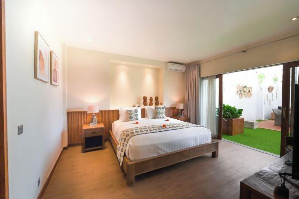 Ein modernes Hotelzimmer mit einem großen Bett, Nachttischen, einem kleinen Schreibtisch und Blick auf eine grüne Außenanlage.