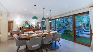 Comedor con una mesa grande dispuesta para seis personas, sillas alrededor y vistas a un jardín exuberante a través de amplios ventanales correderas.