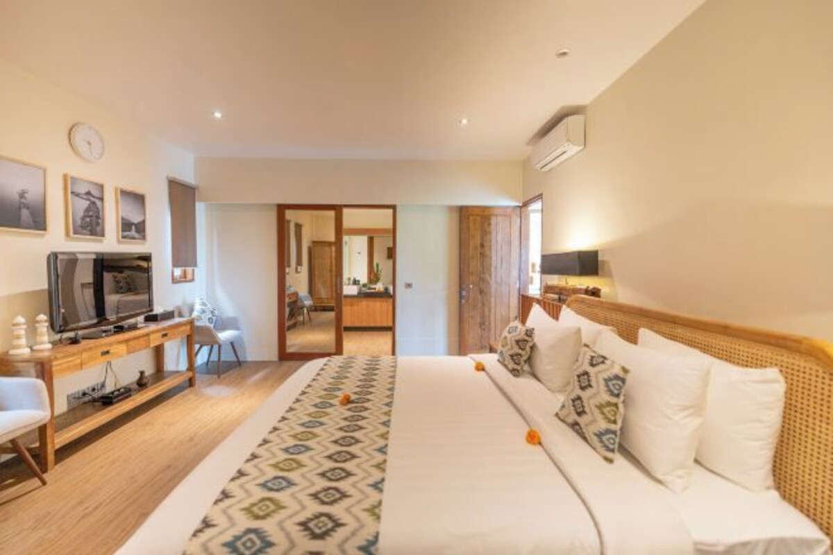 Une chambre d’hôtel avec un lit, une télévision, un bureau et une chaise. Une porte donne accès à une autre pièce.
