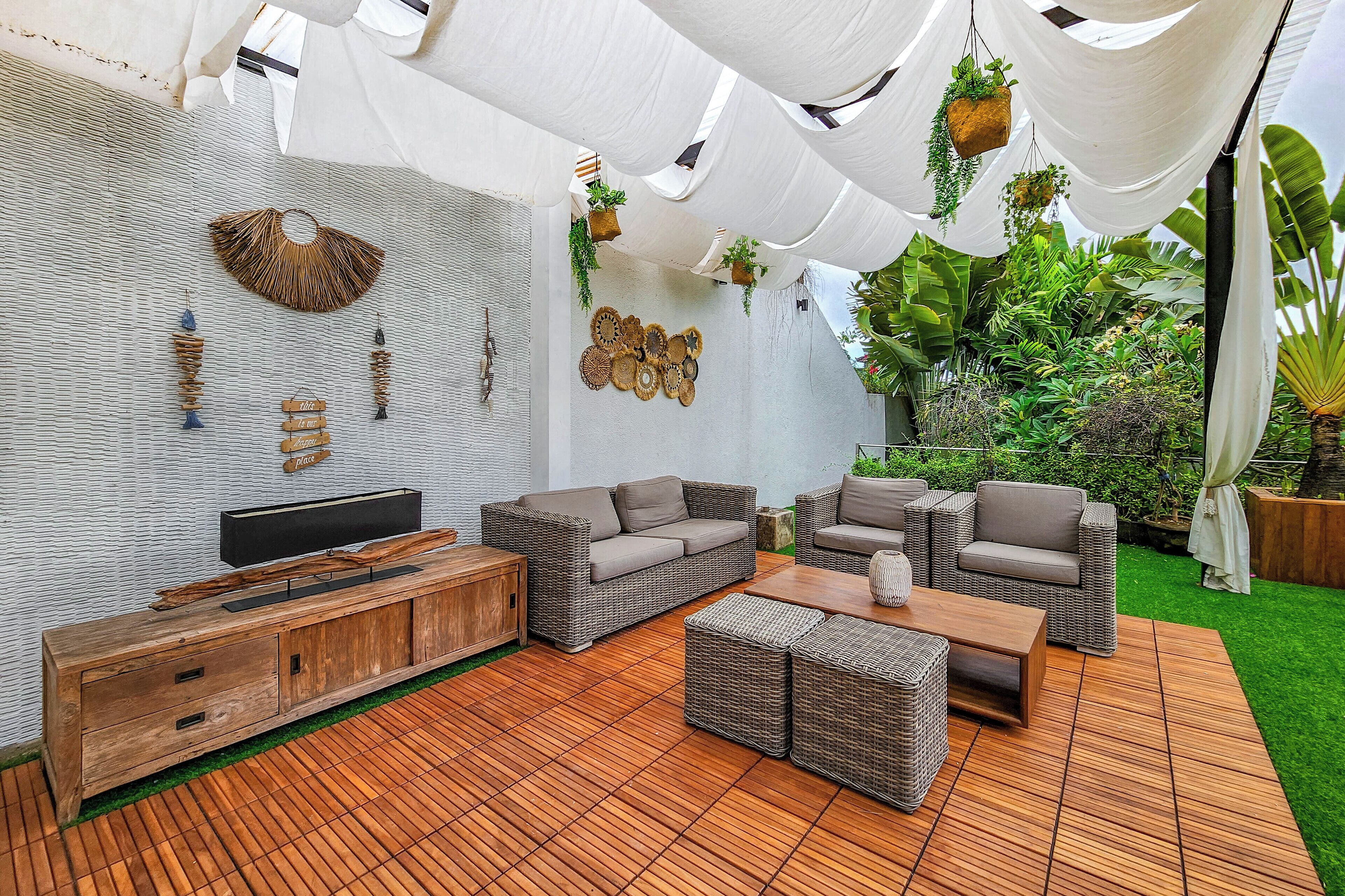 A modern outdoor living area with wicker furniture, a wooden cabinet, and hanging plants.