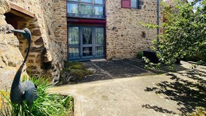 A stone building with a red window shutter, a small window with a red shutter, and a stone wall with a circular window.