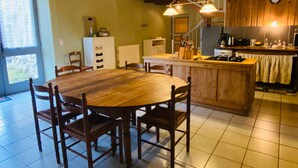 A wooden dining table with chairs, a kitchen area with a stove, and a window with curtains.