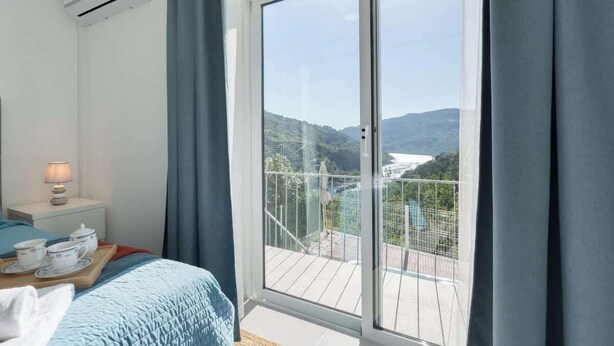 Une chambre dotée d’une grande porte-fenêtre coulissante donnant sur un balcon avec vue sur une rivière et des collines.