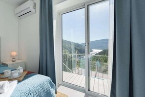 Quarto com uma grande porta de correr de vidro que dá para uma varanda com vista para um rio e colinas.