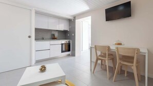 Une cuisine moderne avec des armoires blanches, un four encastré et un coin repas comprenant deux chaises en bois et une table blanche.