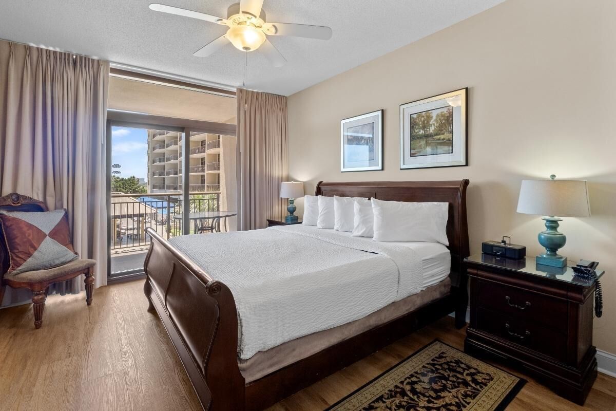 Een hotelkamer met een groot bed, een nachtkastje met een lamp, een stoel en uitzicht op een balkon.