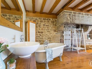 Un baño con pared de piedra, techo de madera y bañera blanca.