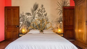 Un dormitorio con una cama grande, dos mesitas de noche con lámparas, un mural tropical en la pared y armarios de madera.