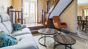 Una sala de estar moderna con un sofá gris, dos mesas redondas y una escalera de madera.