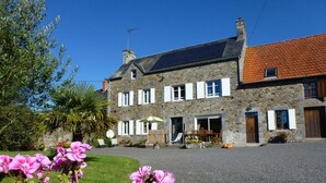 A stone building with a gravel driveway and a garden with pink flowers. - Charming Country House with Private Spa, Fireplace, and Family-Friendly Amenities (Bricqueville-la-Blouette)