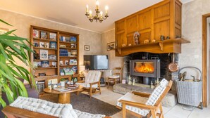 A cozy living room with a fireplace, wooden furniture, and a bookshelf filled with books. - Charming Country House with Private Spa, Fireplace, and Family-Friendly Amenities (Bricqueville-la-Blouette)