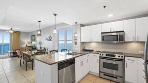 A modern kitchen with stainless steel appliances, white cabinetry, and a central island with a dishwasher. - Grand Panama 1801! Sunset Views, Corner Unit, Pets OK (Panama City Beach)