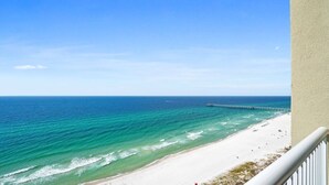 A beach view with clear blue water, a sandy shore, and a pier extending into the ocean. - Grand Panama 1801! Sunset Views, Corner Unit, Pets OK (Panama City Beach)