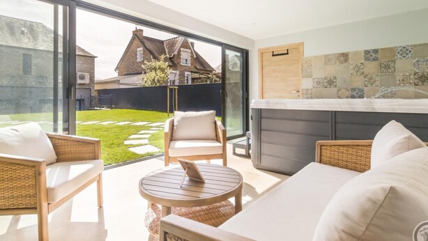 A modern living room with a glass wall, wicker furniture, and a view of a house.