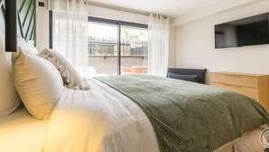 A modern bedroom with a bed, a TV mounted on the wall, and a view of the outside through a large window.