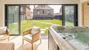 A modern outdoor area with a hot tub, wicker chairs, and a view of a stone building.