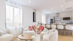 A modern living room with a sofa, chairs, a coffee table, and a kitchen in the background.