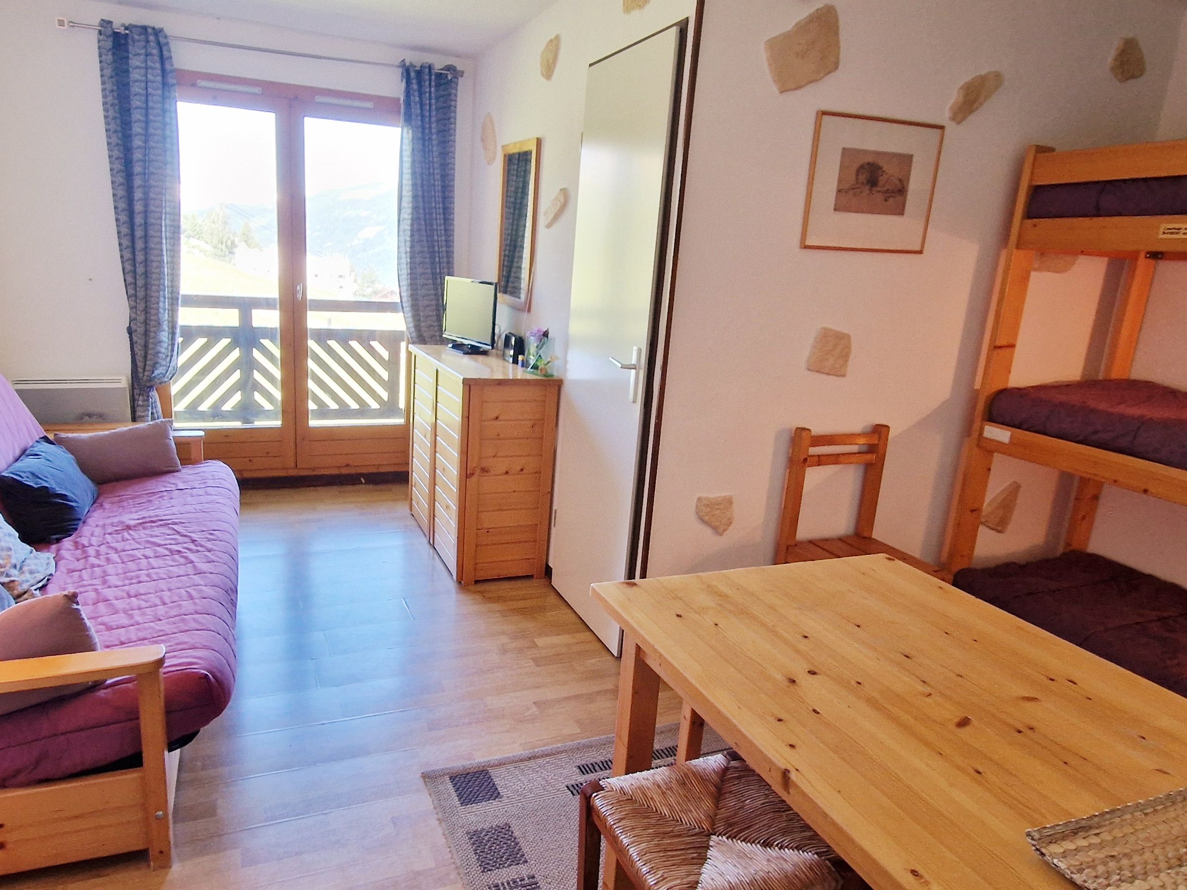 Ein Zimmer mit einem Holzbett, einer Couch mit Kissen, einem Holztisch, einem kleinen Schrank und einem Spiegel an der Wand.