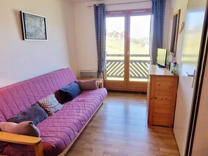 Une pièce chaleureuse avec un canapé rose, un meuble en bois et une grande fenêtre avec des rideaux.