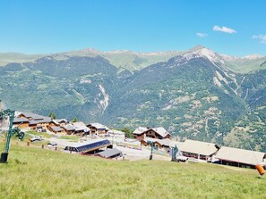 A mountainous village with traditional wooden houses, a ski lift, and a clear view of the surrounding peaks.