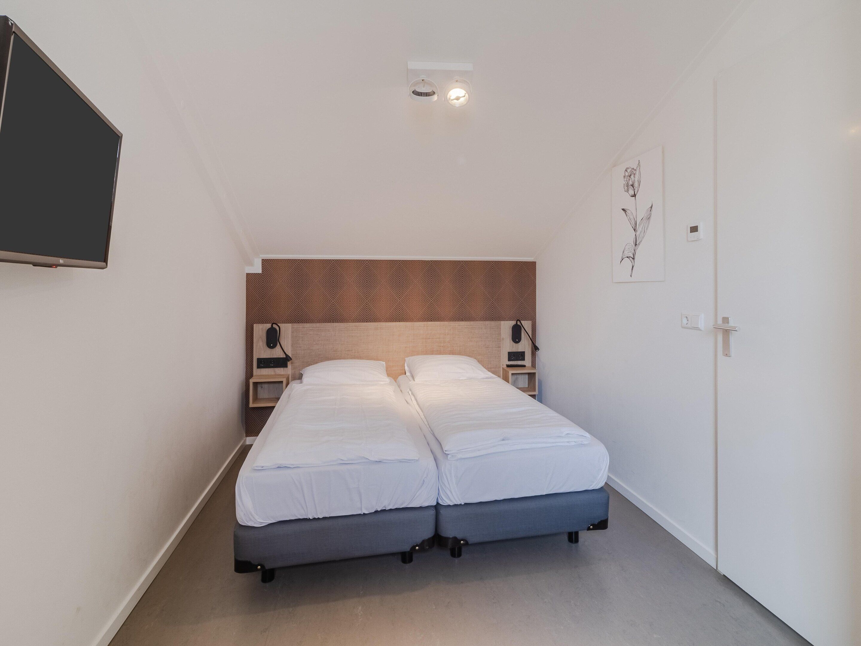 A small, modern bedroom with a bed, bedside tables, and a mounted TV.