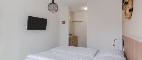 A bedroom with a bed, a television mounted on the wall, a hanging light fixture, and a bathroom visible through an open door.