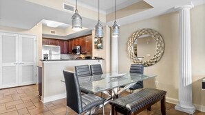 Una cocina moderna con electrodomésticos de acero inoxidable, una mesa de comedor de cristal con sillas y un espejo decorativo en la pared.
