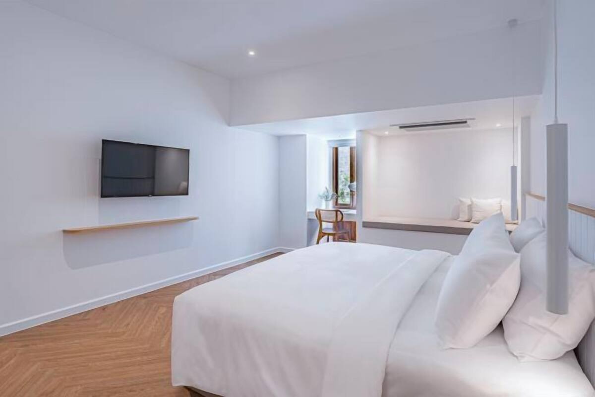 A modern hotel room with a bed, a mounted TV, a desk, and a chair.