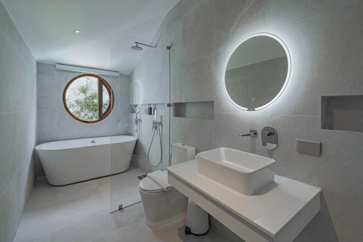 Un baño moderno con una bañera independiente, un lavamanos rectangular y un espejo redondo.