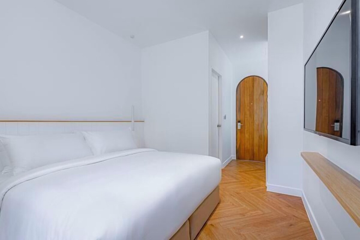 Un dormitorio con una cama, suelo de madera, una puerta de madera y un espejo grande.