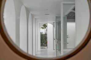 A corridor with a view through a circular window, leading to a door.