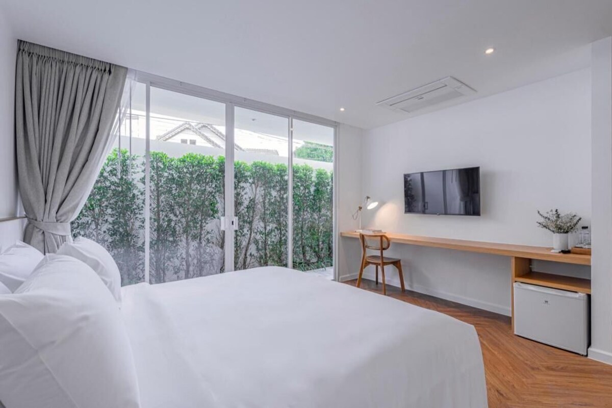 A modern hotel room with a large bed, a desk with a chair, a television, and a small refrigerator.