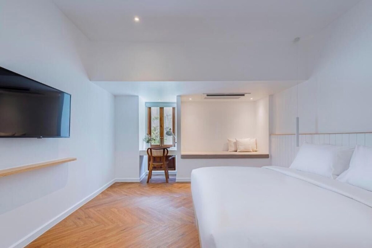 A modern hotel room with a large bed, a mounted TV, a small desk, and a window.