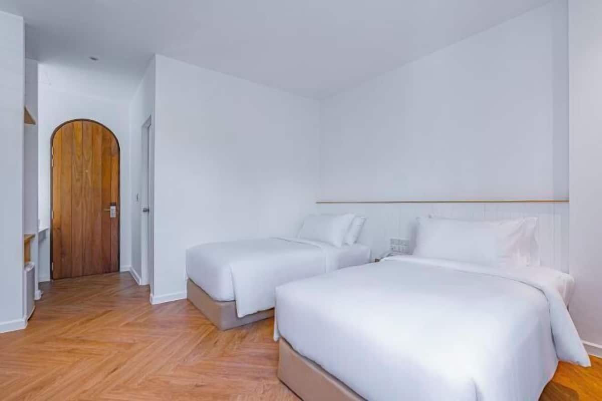 A bedroom with two beds, a wooden door, and a white wall.