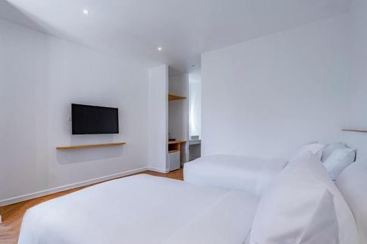 Une chambre à coucher moderne avec un lit, un téléviseur à écran plat fixé au mur et une étagère en bois.