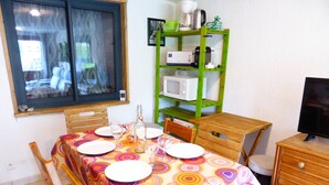 Un comedor con una mesa dispuesta para cuatro, una estantería verde con electrodomésticos de cocina y un televisor sobre un mueble de madera.