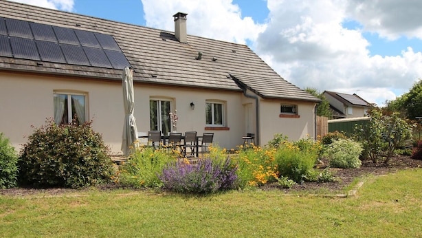 A house with a solar panel roof, a patio with outdoor furniture, and a garden with various plants and flowers. - Charming Family-Friendly Cottage, Pet Welcome, Garden, Near Blois & Loire Castles (Valencisse-Chambon-sur-Cisse)