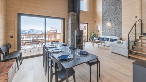 A spacious dining area with a large table set for six, a stone fireplace, and a balcony with a view of snow-capped mountains. - 125m² Ski-In Duplex with PARKING, 4 Bedrooms (Huez)