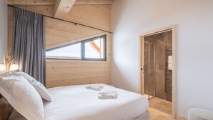 A bedroom with a wooden ceiling, a bed with white bedding, a window with curtains, and a walk-in closet. - 125m² Ski-In Duplex with PARKING, 4 Bedrooms (Huez)