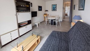 Ein modernes Wohnzimmer mit Sofa, Esstisch mit Stühlen, einer Küchenzeile und einem an der Wand befestigten Fernseher.