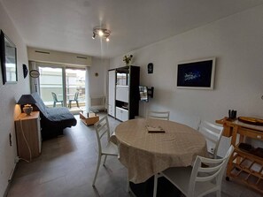 Un espacio habitable compacto con comedor, kitchenette y un pequeño balcón.