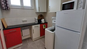 Eine kleine Küche mit weißen Schränken, einer roten Arbeitsplatte, einem weißen Kühlschrank und einer Mikrowelle.