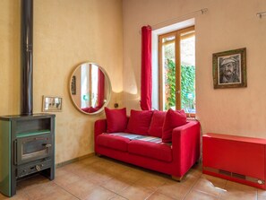 A room with a red sofa, a small heater, a mirror, and a window with red curtains.