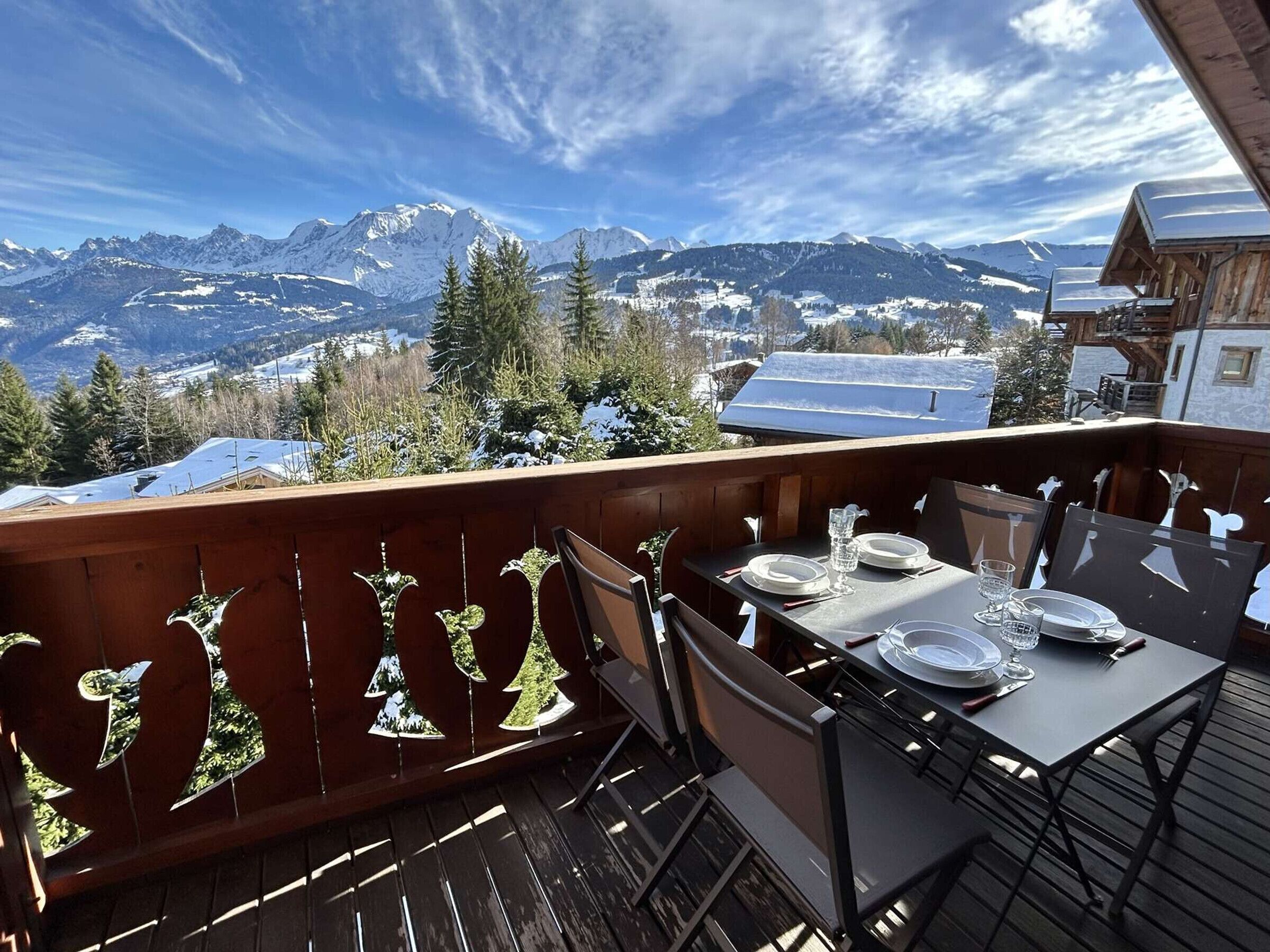 A wooden deck with a table set for two, overlooking a snowy mountain landscape.