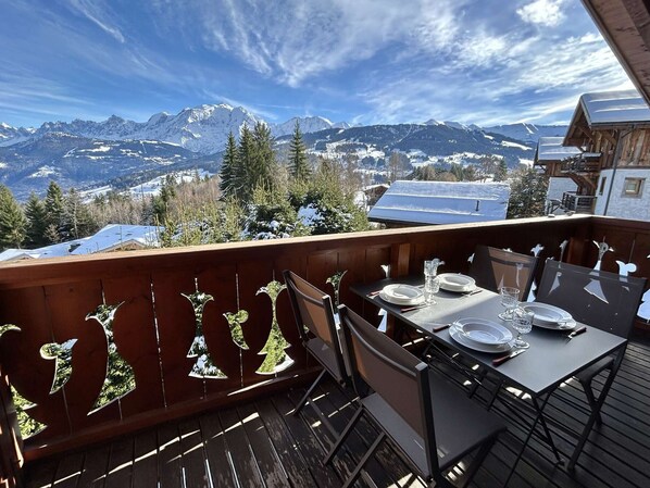 Eine Holzterrasse mit einem für zwei Personen gedecktem Tisch, mit Blick auf eine verschneite Berglandschaft.