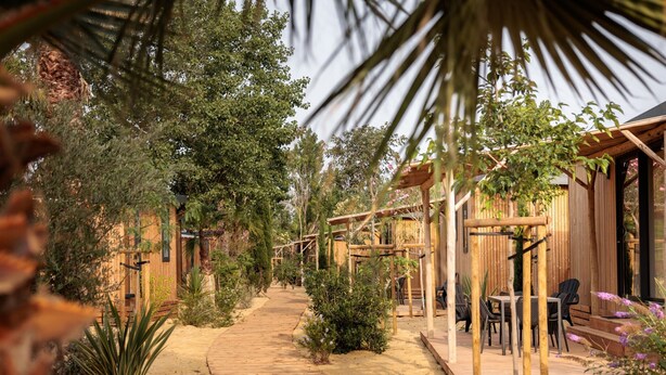 Een houten pad dat leidt naar een rustieke buitenruimte met zitgedeelte, een pergola en stoelen.