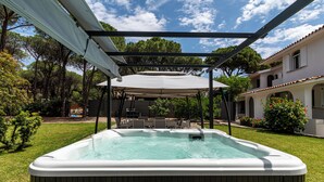 A hot tub under a pergola with a pool and outdoor furniture in the background. - Villa Beachfront Marina (Santa Margherita di Pula)