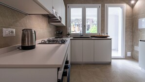A modern kitchen with white cabinets, a gas stove, a kettle, and a window providing natural light. - Villa Beachfront Marina (Santa Margherita di Pula)