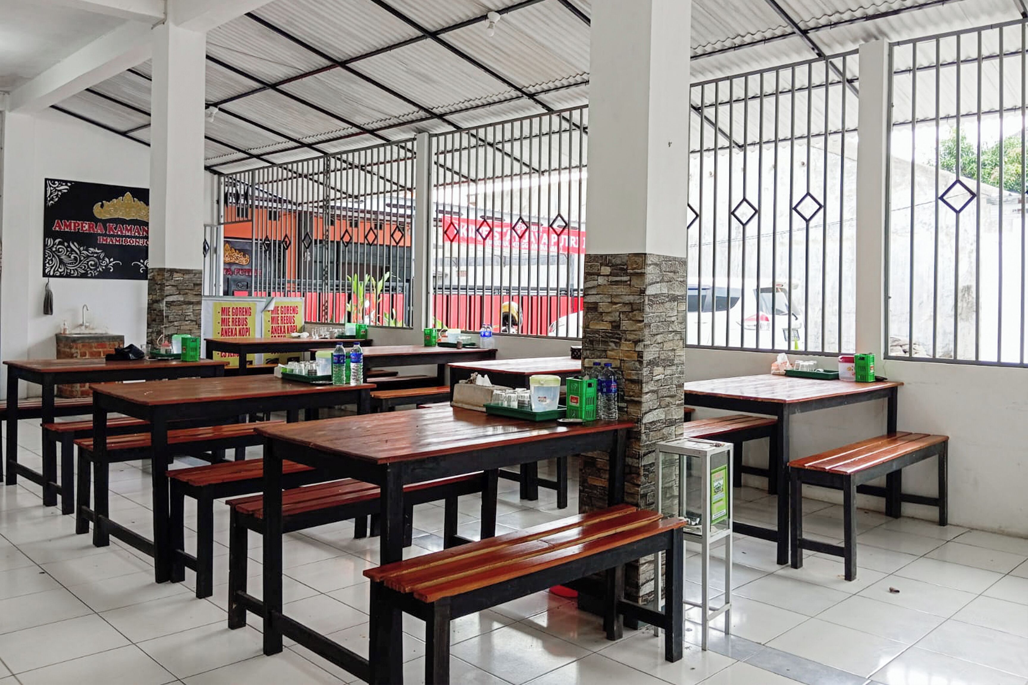 Un restaurant avec des tables et des bancs en bois, un pilier en pierre et une vue à travers des barreaux métalliques.