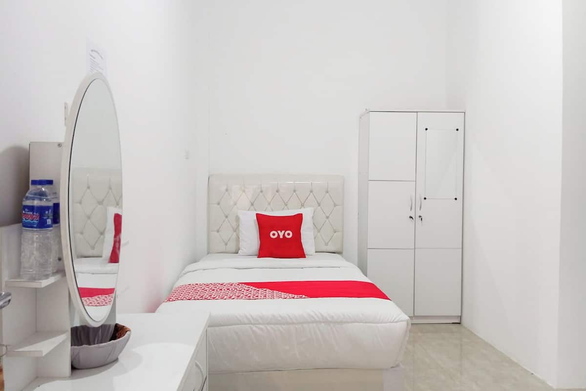 A hotel room with a bed, a wardrobe, a mirror, and a water bottle on a shelf.
